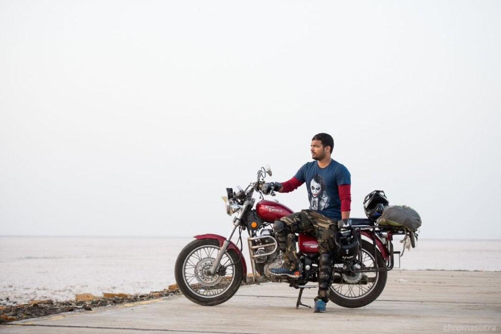 MAN SITTING ON BULLET BIKE ON THE WHITE SALT FLATS OF RANN OF KUTCH IN GUJARAT