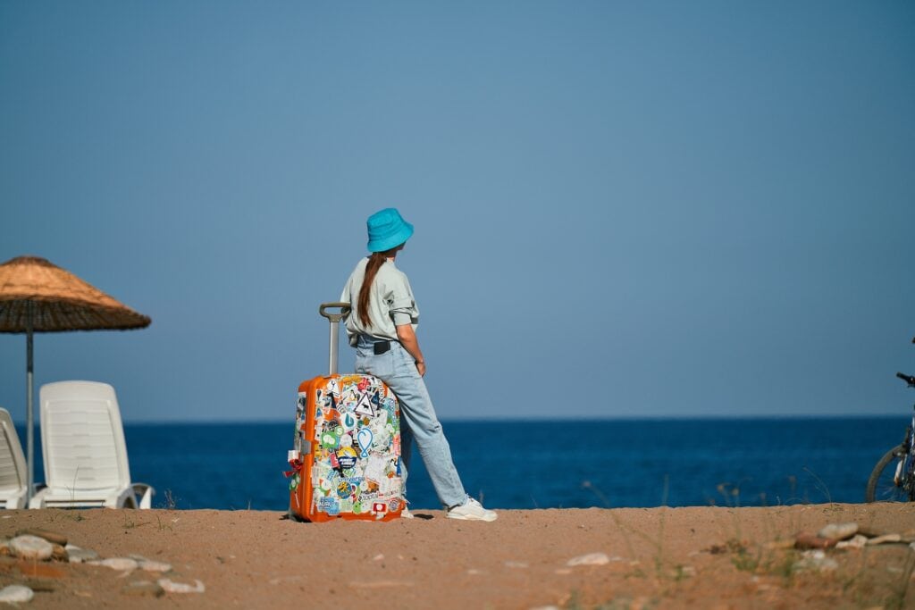 Die Mitarbeiterin eines jungen Startup Unternehmens sitzt im Urlaub auf ihrem Koffer am Strand und blickt auf das Meer.