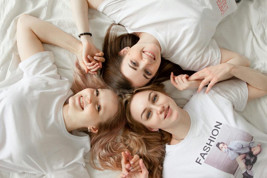Three young women lying on a bed, smiling and enjoying casual moments indoors.