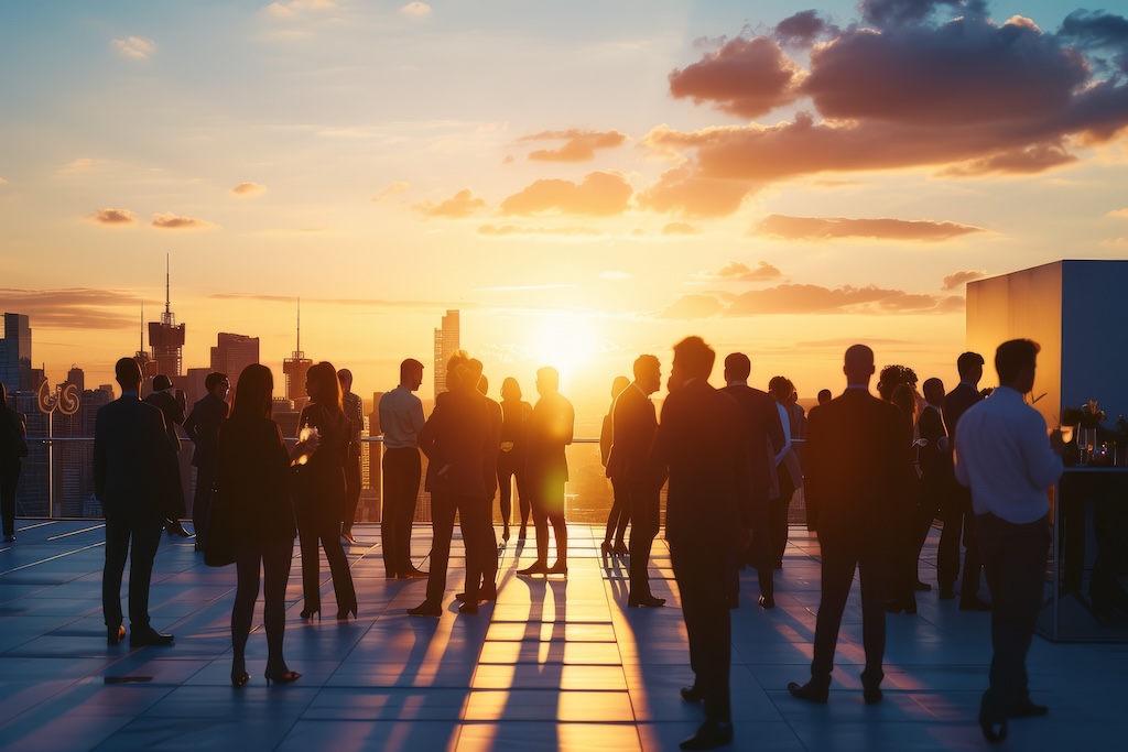 A group of business professionals networking on a rooftop terrace at sunset, with the city skyline in the background, embodying a summer surge of connection and opportunity.
