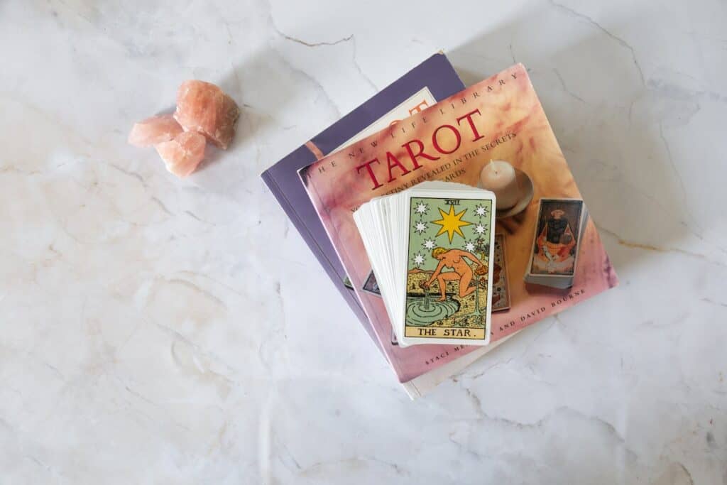 tarot deck pictured on top of tarot book stack alongside rose quartz crystals on a white marble background