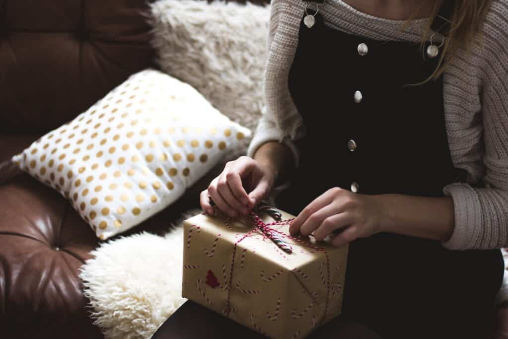 woman in pinafore dress and jumper sat on sofa opening a Christmas gift in candy cane brown wrapping paper