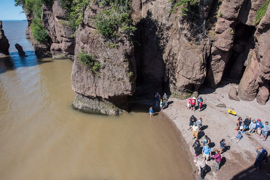 group of tourists on the very small beach that is still walkable at Hopewell Rocks during high tide.