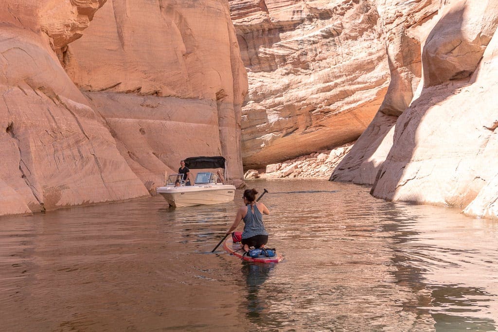 Brooke on her paddleboard on her knees as a boat passes by in the canyon