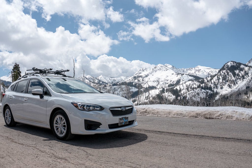 White Subaru Imprezza with snow covered mountains behind it