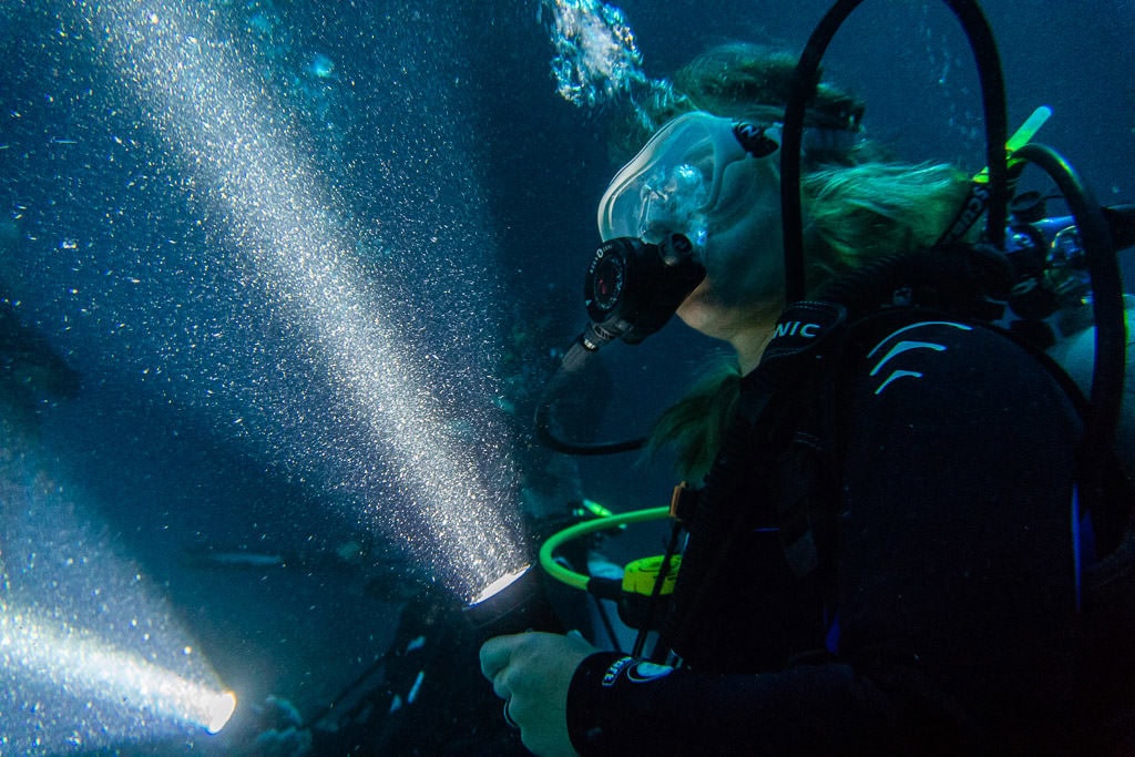 Fellow diver on our tour with Manta Ray Dives of Hawaii holding her flashlight with plenty of plankton swimming in the light beam