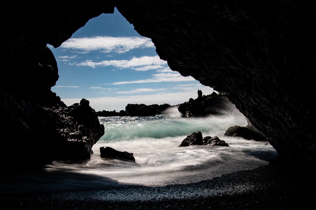 inside the Volcanic Sea Cave looking at the waves crashing outside at the black sand beach in Wai'anapanapa State Park