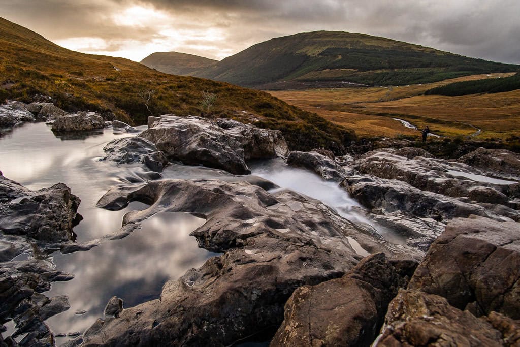 Still water with reflections of clouds in it next to a waterfall at the Fairy Pools in Isle of Skye