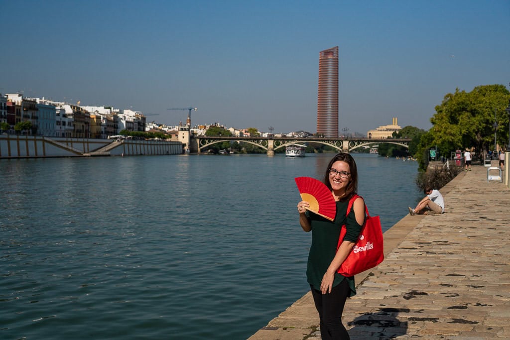 posing with red fan on hot day next to the river in sevilla spain