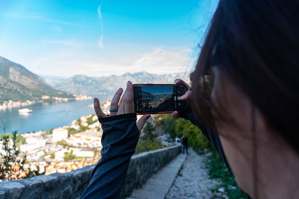 Brooke taking a cell phone photo of the view of Kotor Bay at one of the switchbacks on the way up