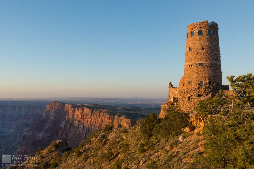 4-story stone tower sits on edge of canyon with views of layered red rocks below the spot which is one of the Grand Canyon South Rim best views
