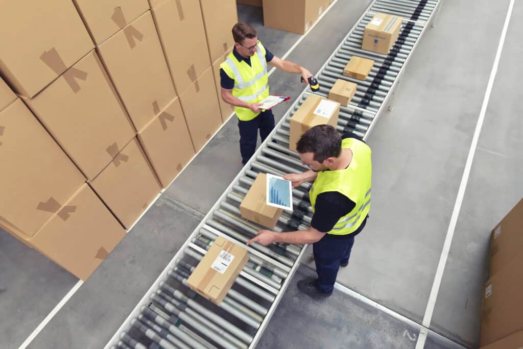 Warehouse workers checking items on a conveyor roller.