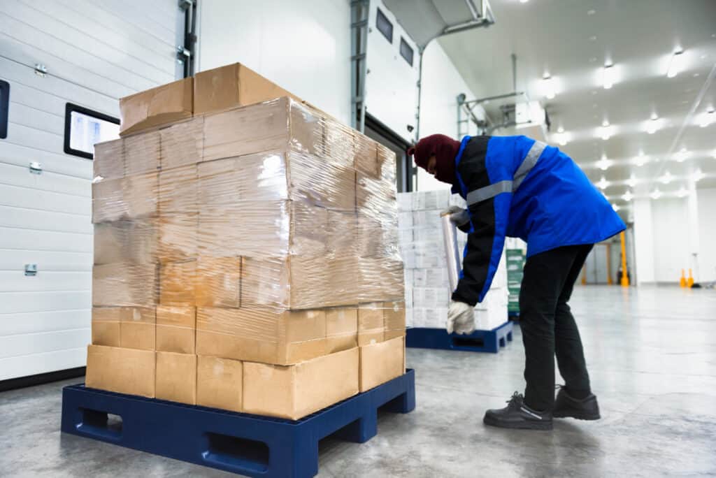 Warehouse freezer worker hand wrapping a pallet.