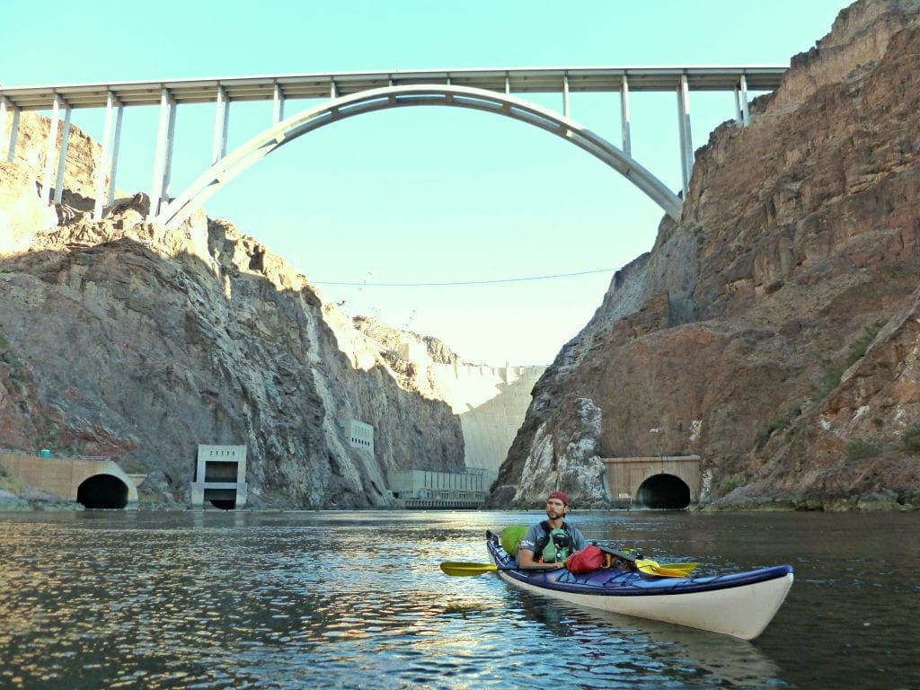 Guide Gary sits in kayak on the Colorado River with the Hoover Dam and Pat Tillman Bridge looming above