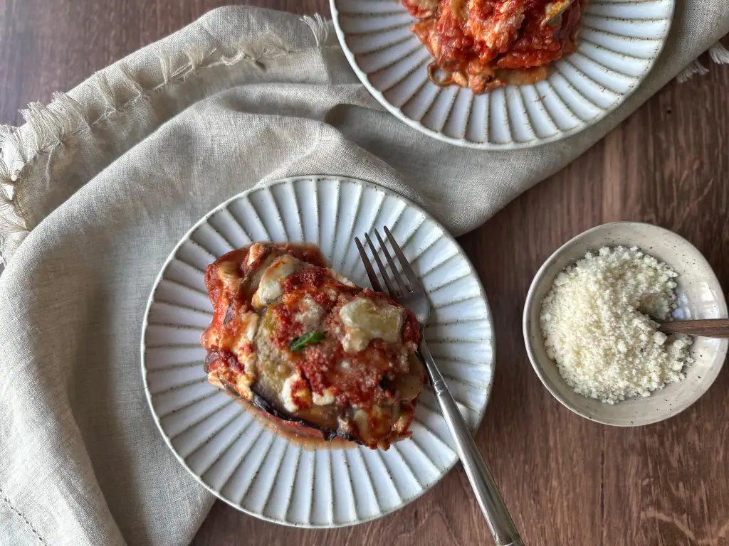 Eggplant Parmesan on a plate with a bowl of cheese on the side.