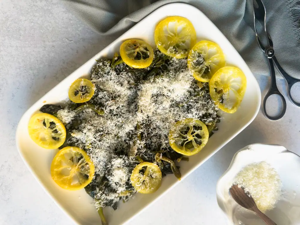 Spinach plated with lemon slices on top and a sprinkle of Parmesan cheese.