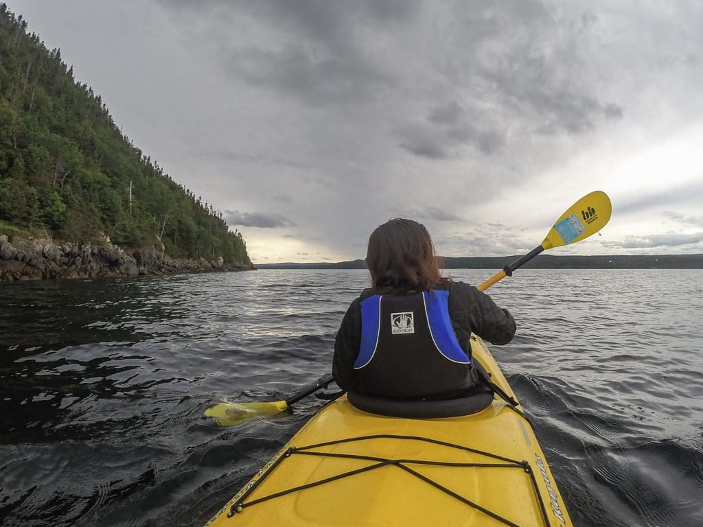 Brooke paddling near a cliff of large trees