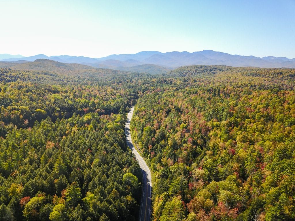 Drone shot of the road surrounded by bright trees with the vermont mountains in the background