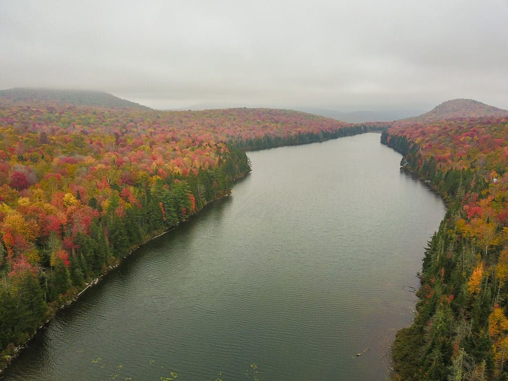 Drone shot of a large lake on a gloomy day surrounded by colorful trees in Groton State Forest