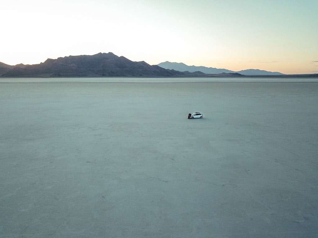 Drone shot of Brooke and Buddy leaning up against the Subaru at the Bonneville Salt Flats with no-one around them