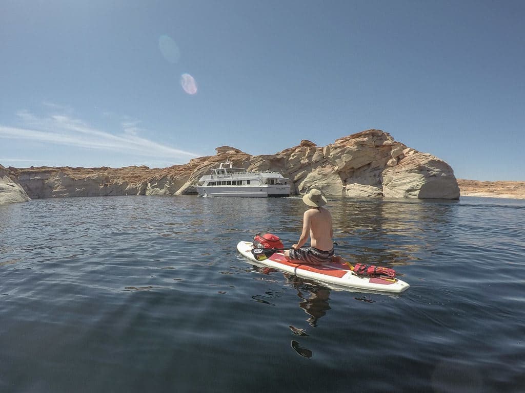 Buddy sitting on his paddleboard on Lake Powell as a tour boat passes in the background