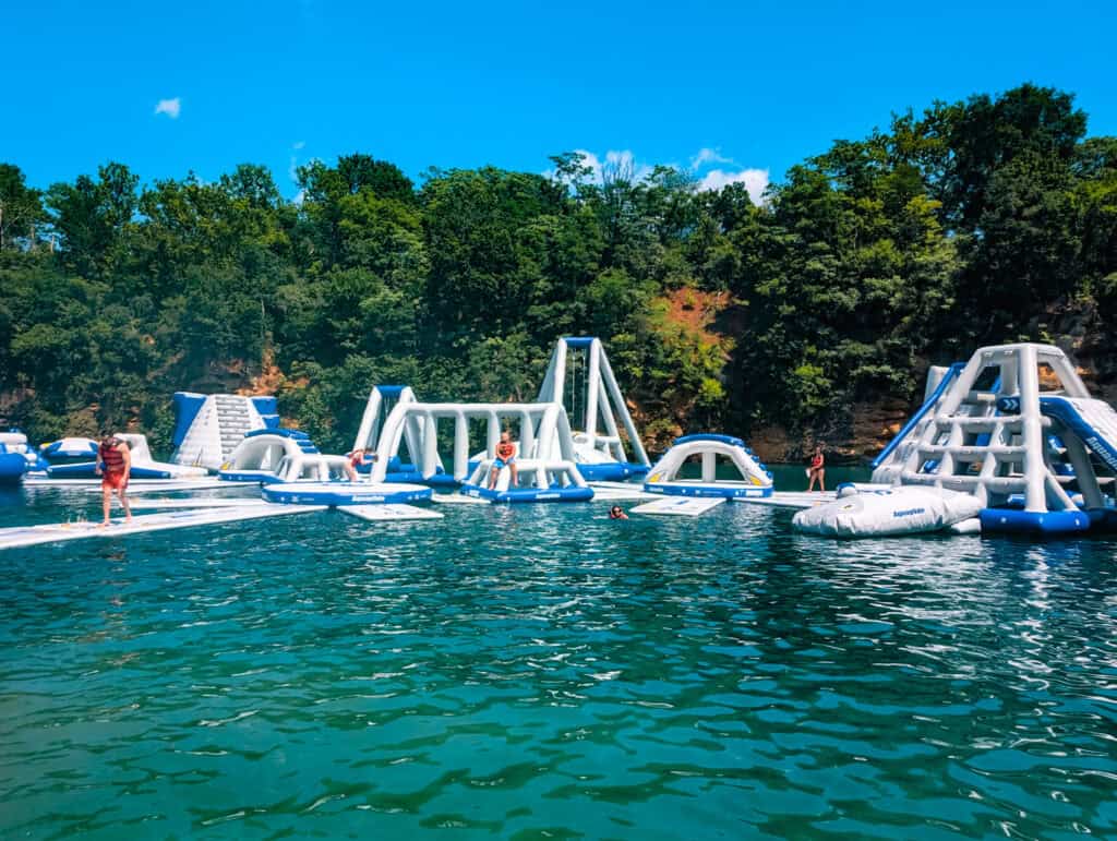 wide shot of inflatable water obstacle course at Harpers Ferry Waterpark, surrounded by trees and blue skies