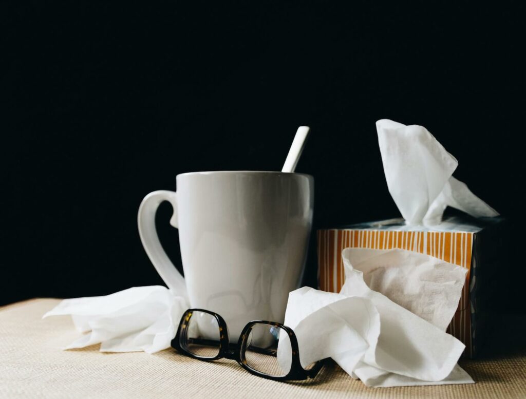 Die digitale Krankmeldung wird durch eine Tasse Tee, gebraucht Taschentücher und eine abgelegte Brille symbolisiert.