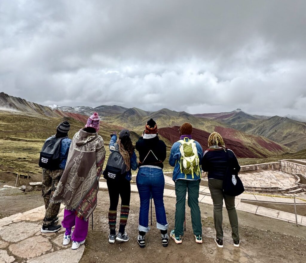 Traveling Black Women viewing the View of the Andes from the road to Palccoyo Rainbow Mountain with llamas grazing along the hillsides.