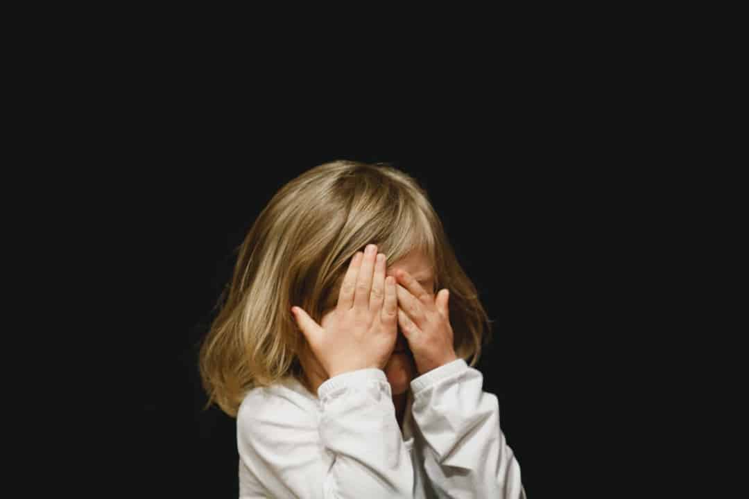 black background, a child is hiding behind her hands