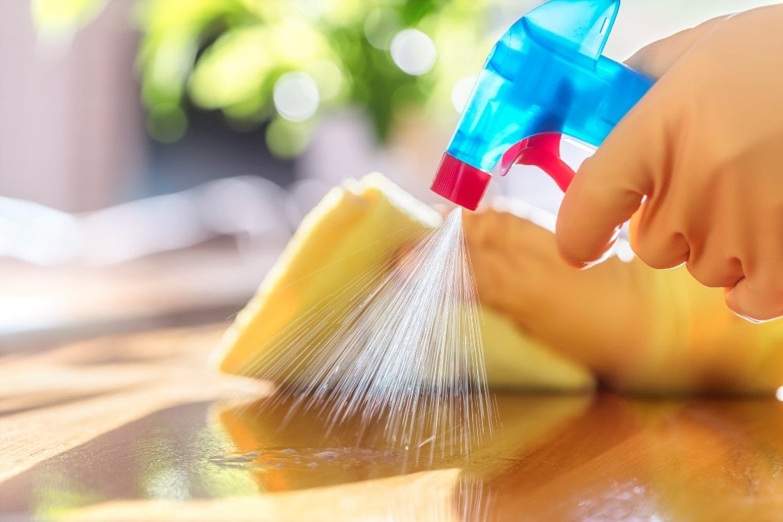 A person wearing yellow gloves spraying cleaning liquid on the table