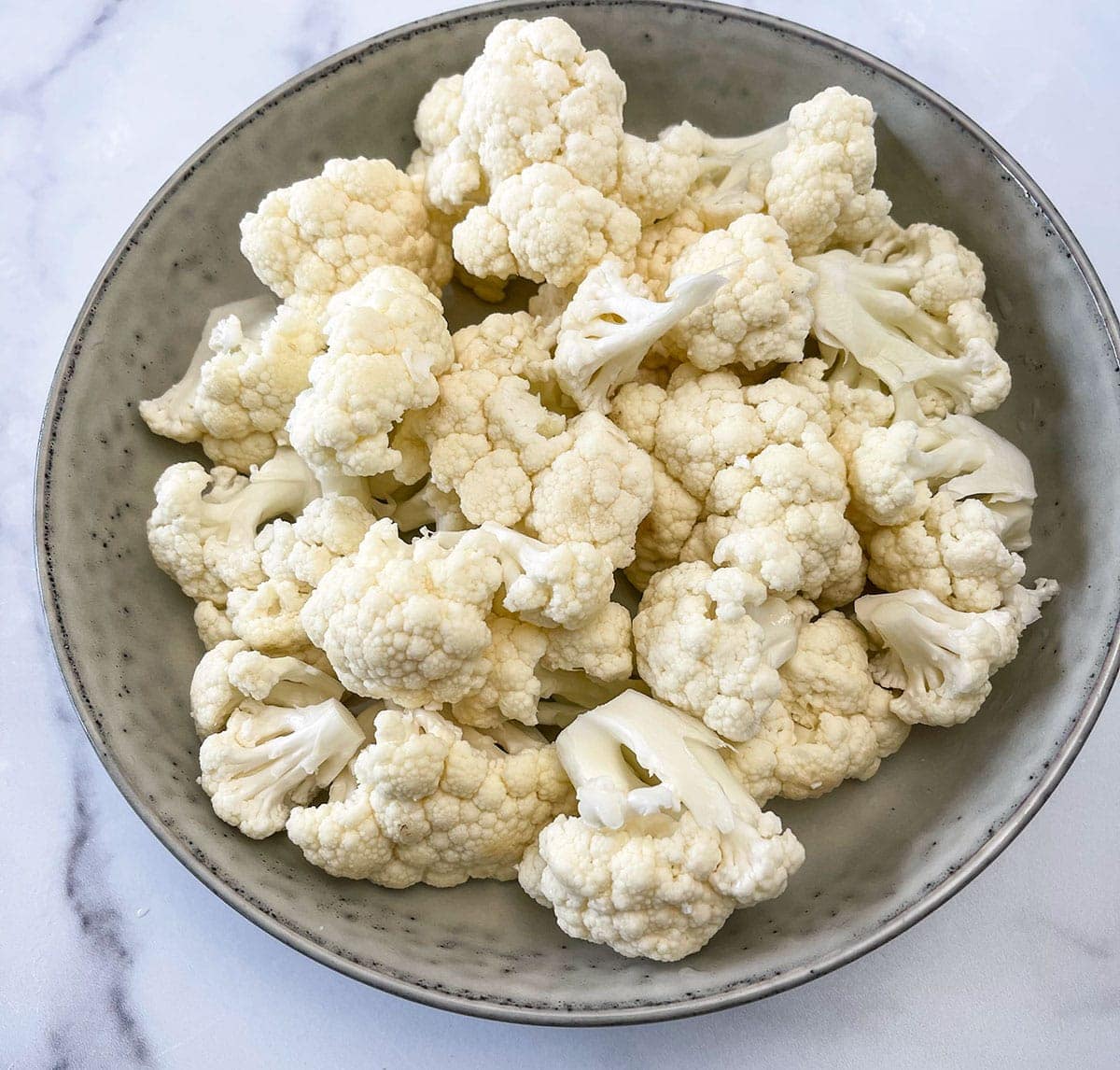 cut cauliflower florets in a beige bowl on a white background