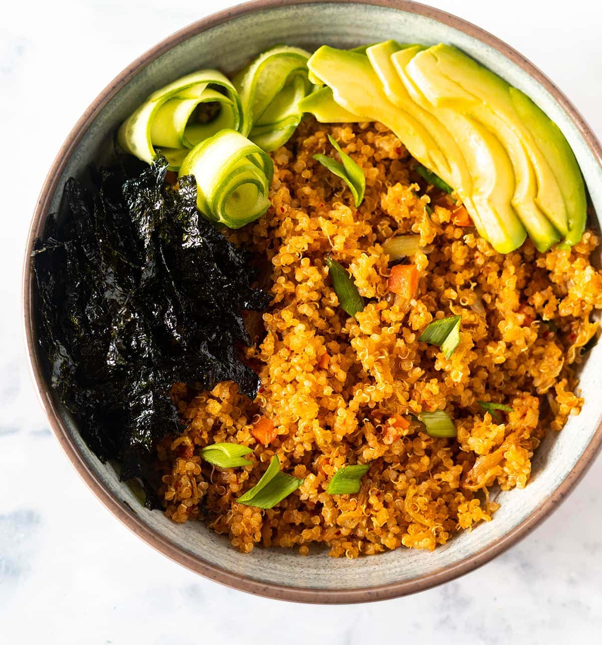 Close up kimchi fried quinoa in a beige bowl with avocado slices, nori strips and cucumber roses