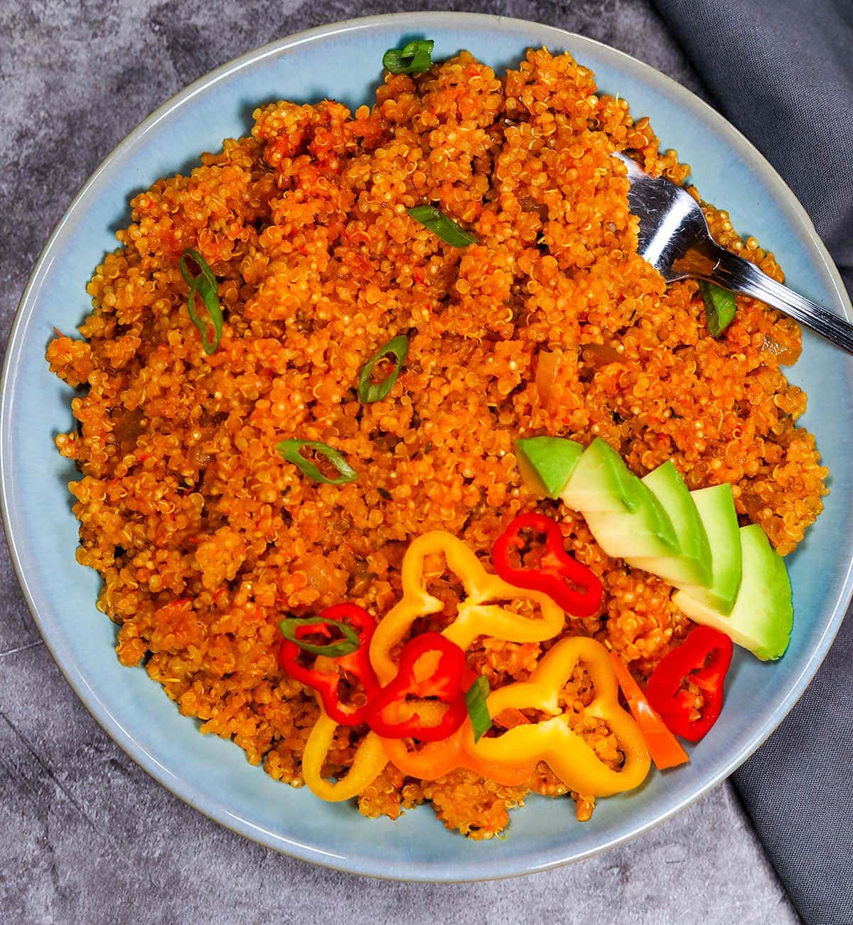 close up image of Jollof Quinoa in a blue bowl on a grey background
