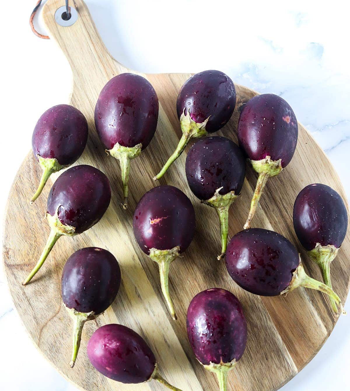 12 baby eggplants on cutting board for making baby eggplant coconut curry