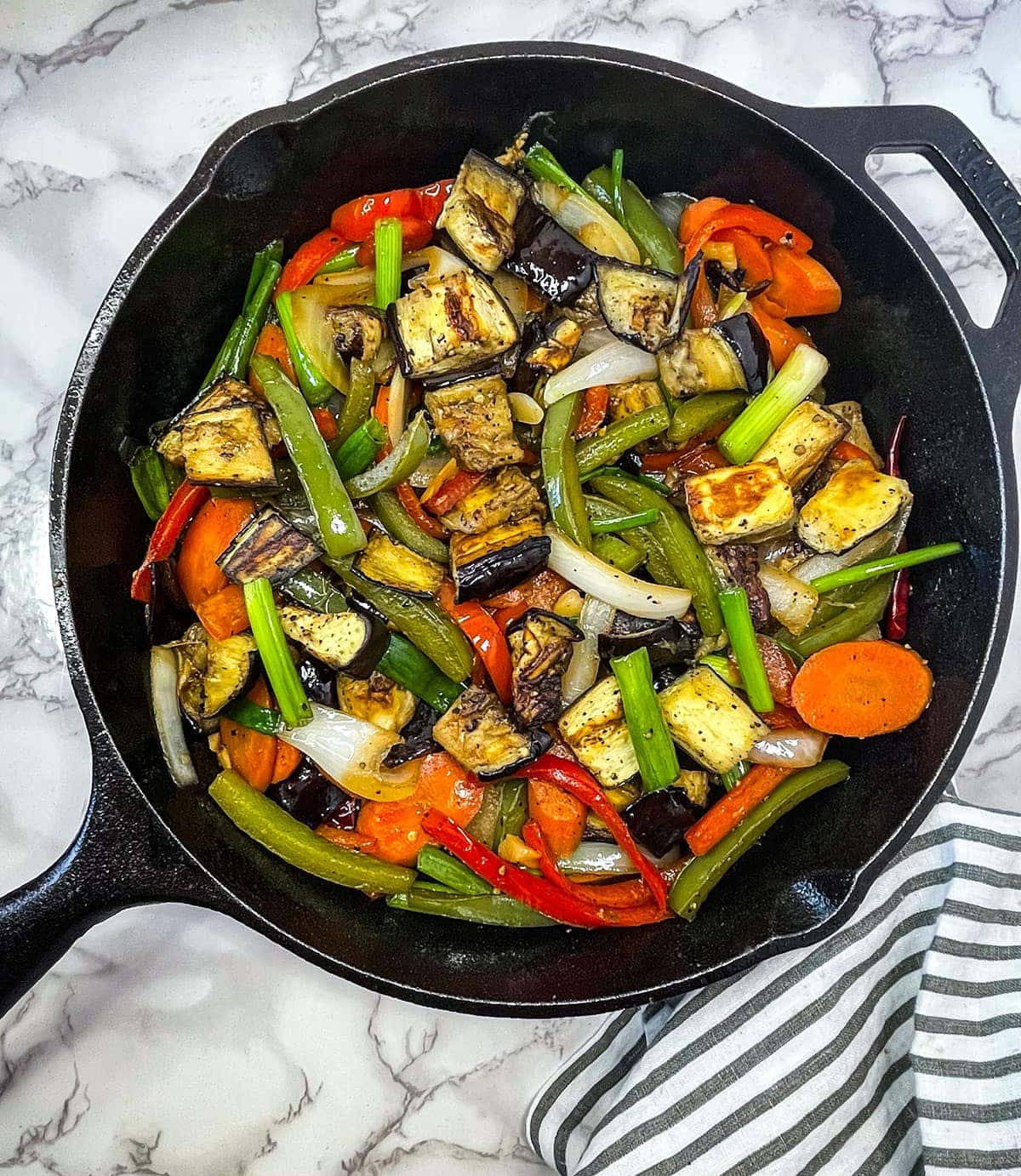 eggplant stir fry in a cast iron skillet on a white marbled background