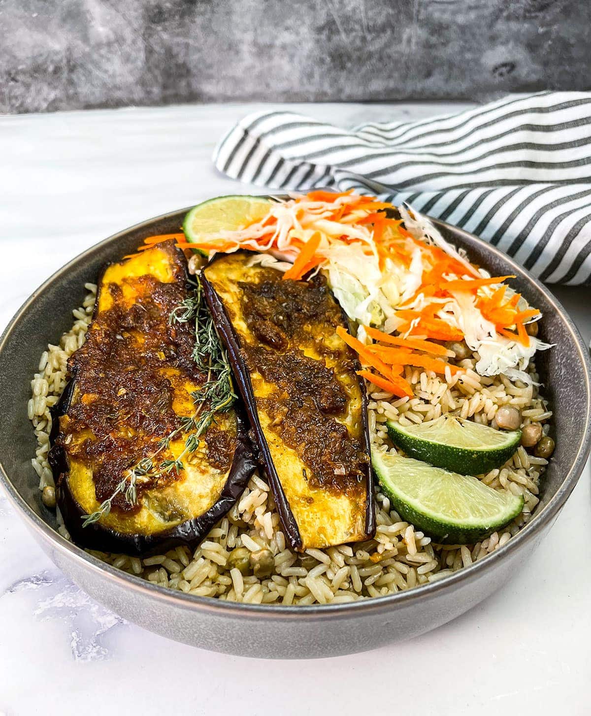 close up broiled eggplant with jerk sauce in a grey bowl with rice and peas and coleslaw