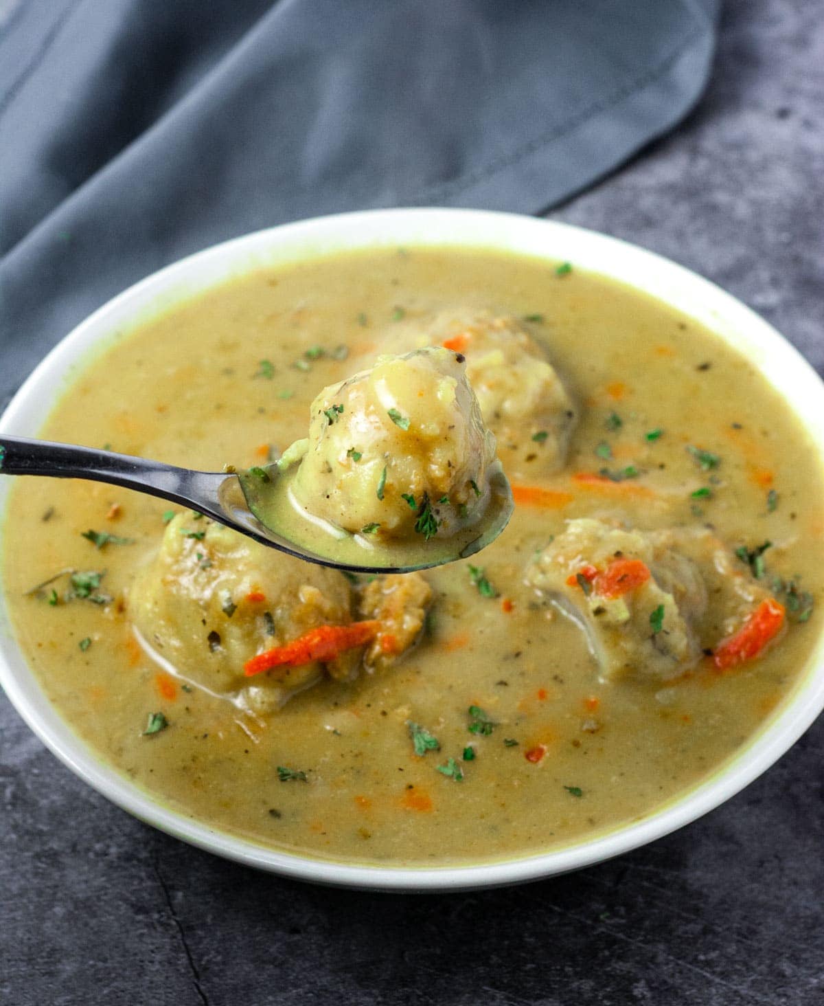 Vegan chicken and dumplings over showing 4 gluten-free vegan dumplings in a white bowl with a spoon