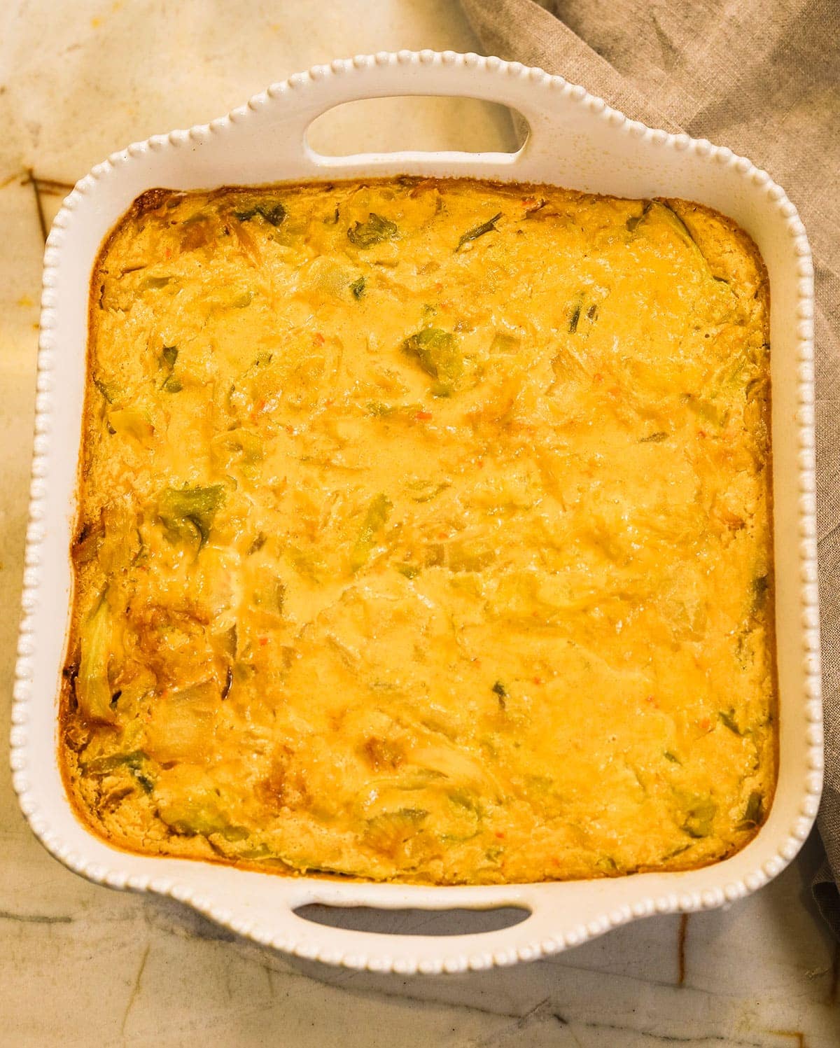 overlay vegan cabbage casserole in a while casserole pan on a marble beige background
