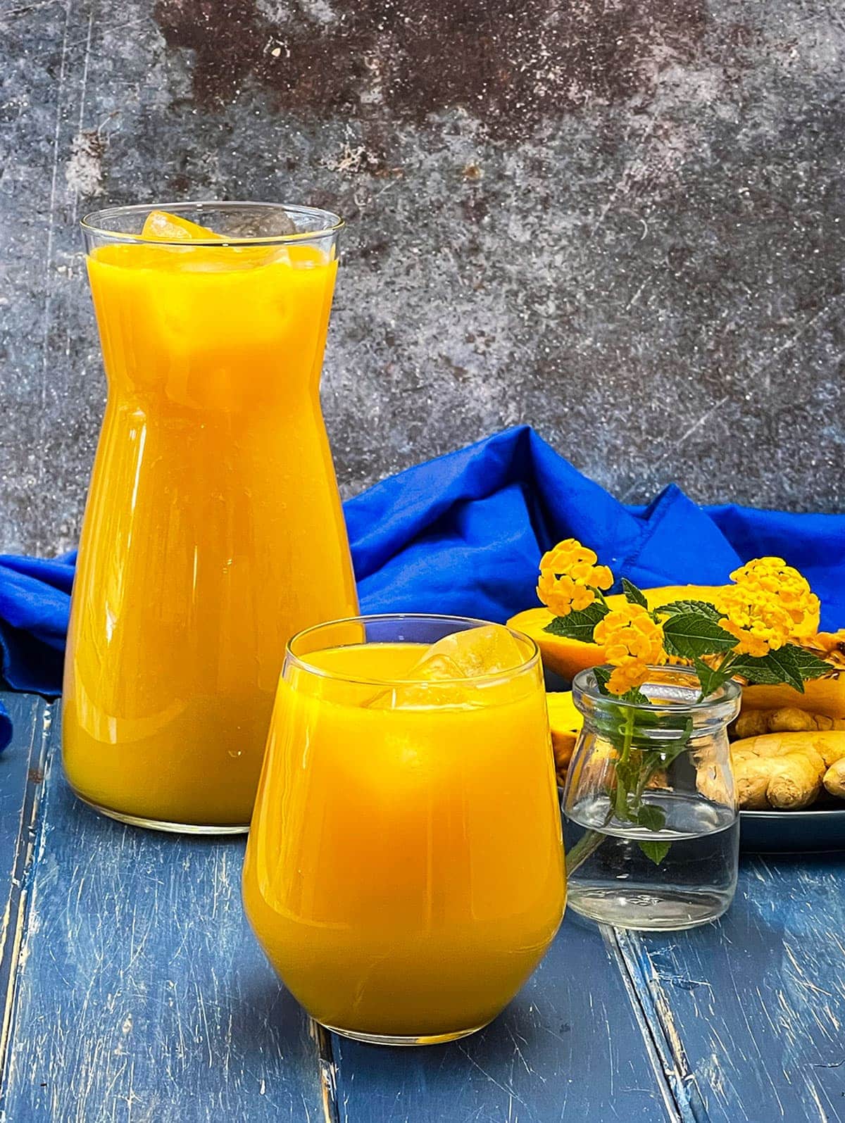 mango pineapple juice in a flask and glass on a blue wooden background with a blue napkin