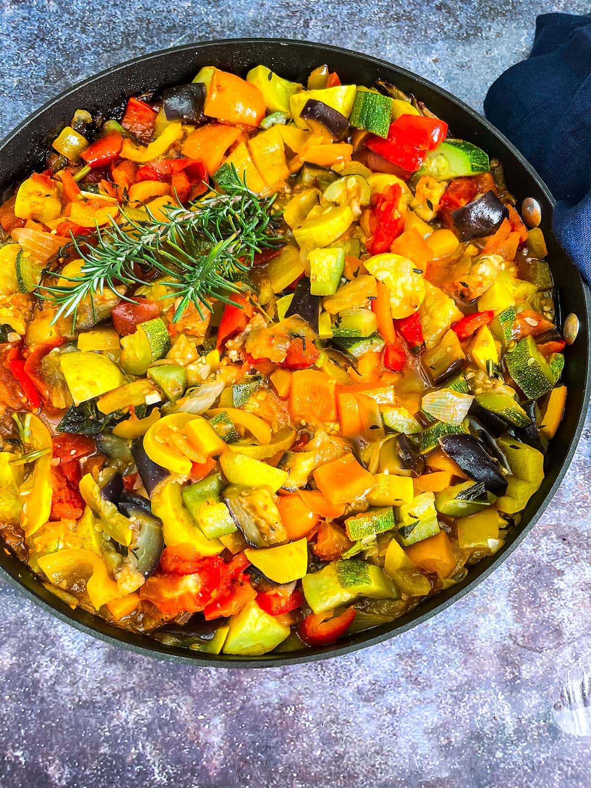 overlay vegan ratatouille with eggplant, zucchini, bell pepper, onion, garlic in a white bowltomato,