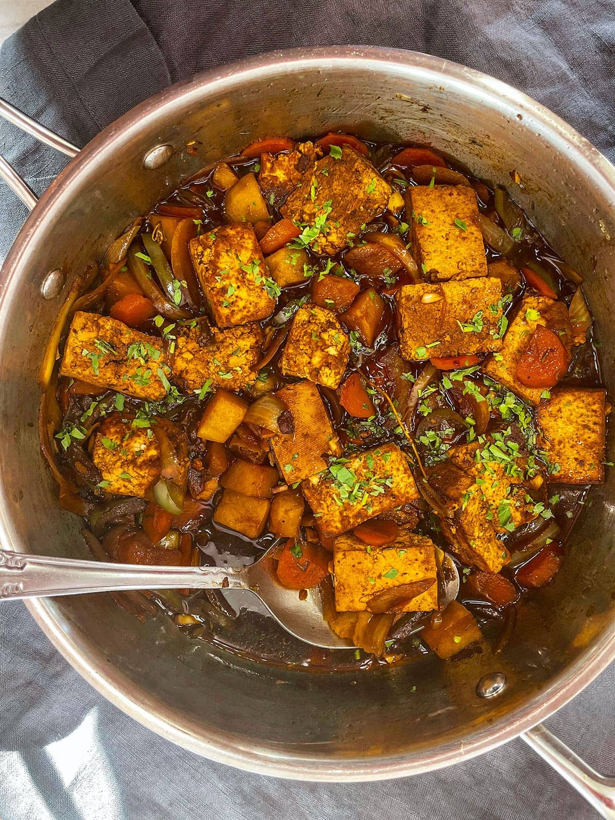 brown stew tofu in saucepan with spoon on grey background