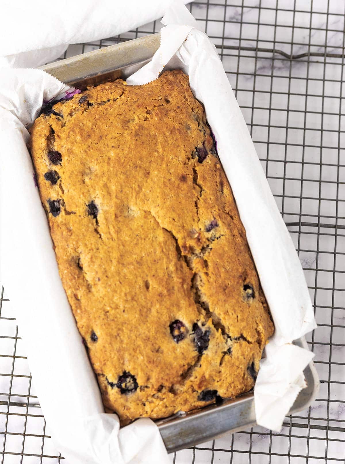 overlay of gluten-free vegan banana bread in a pan lined with parchment paper on a wire rack