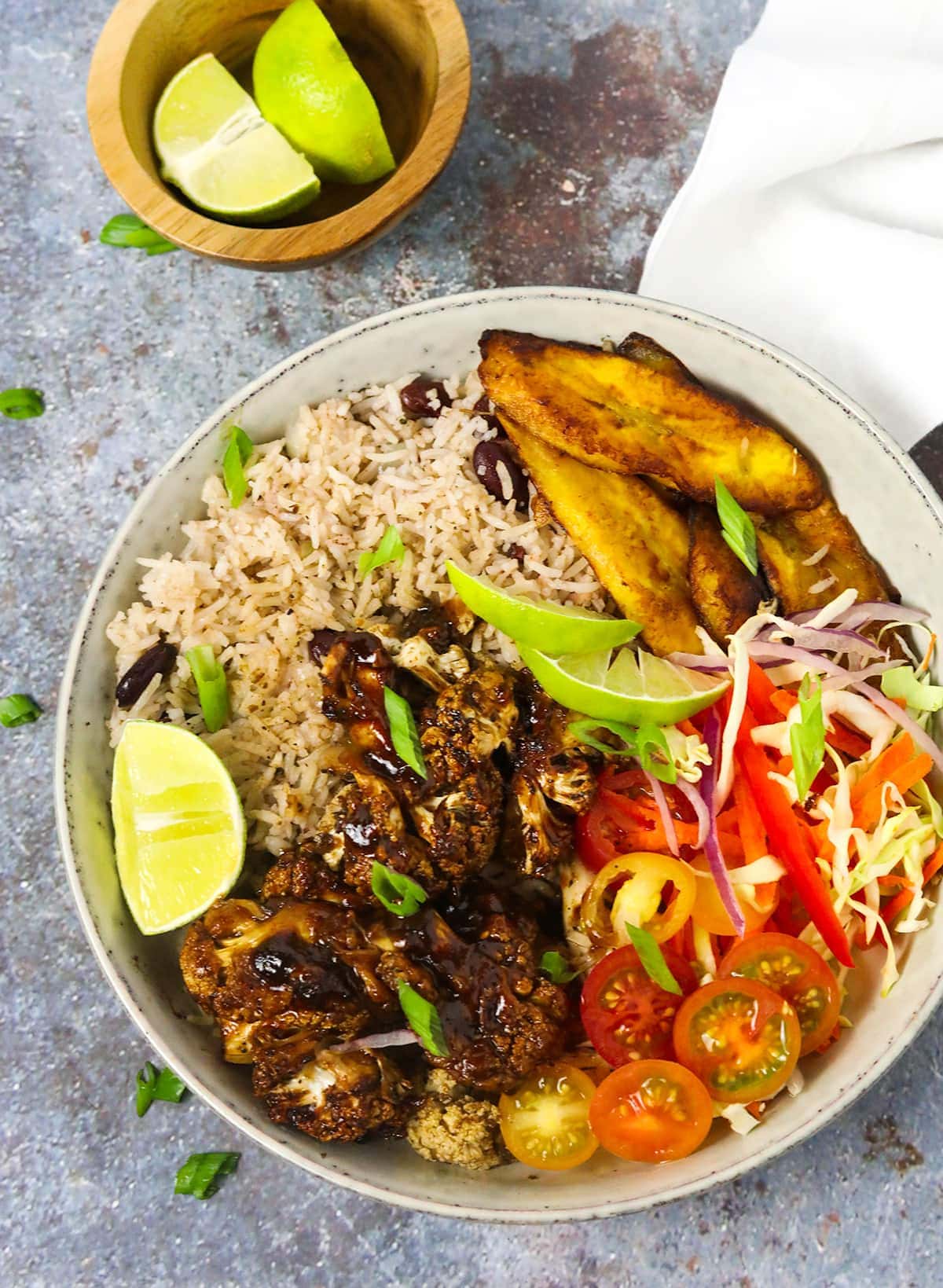 Overlay of bowl with jamaican jerk cauliflowerk rice, plantains on a grey background