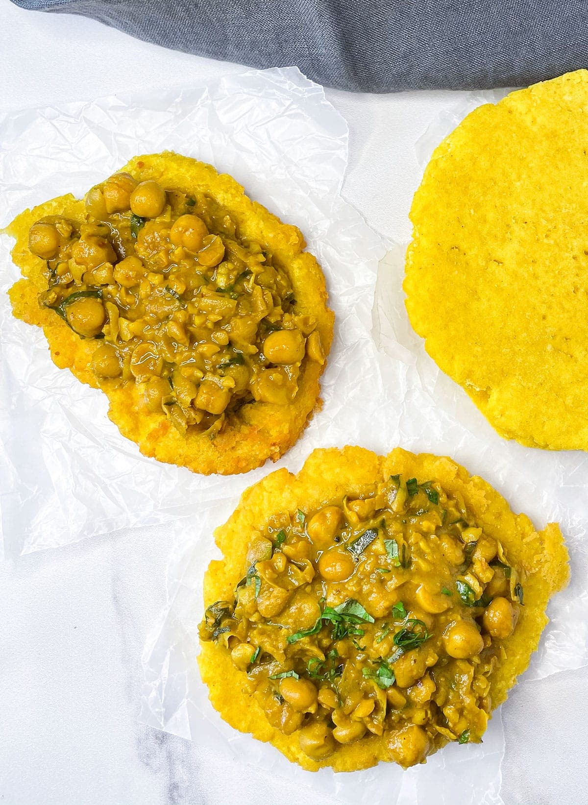overlay of doubles flatbread topped with curry chana on a white background