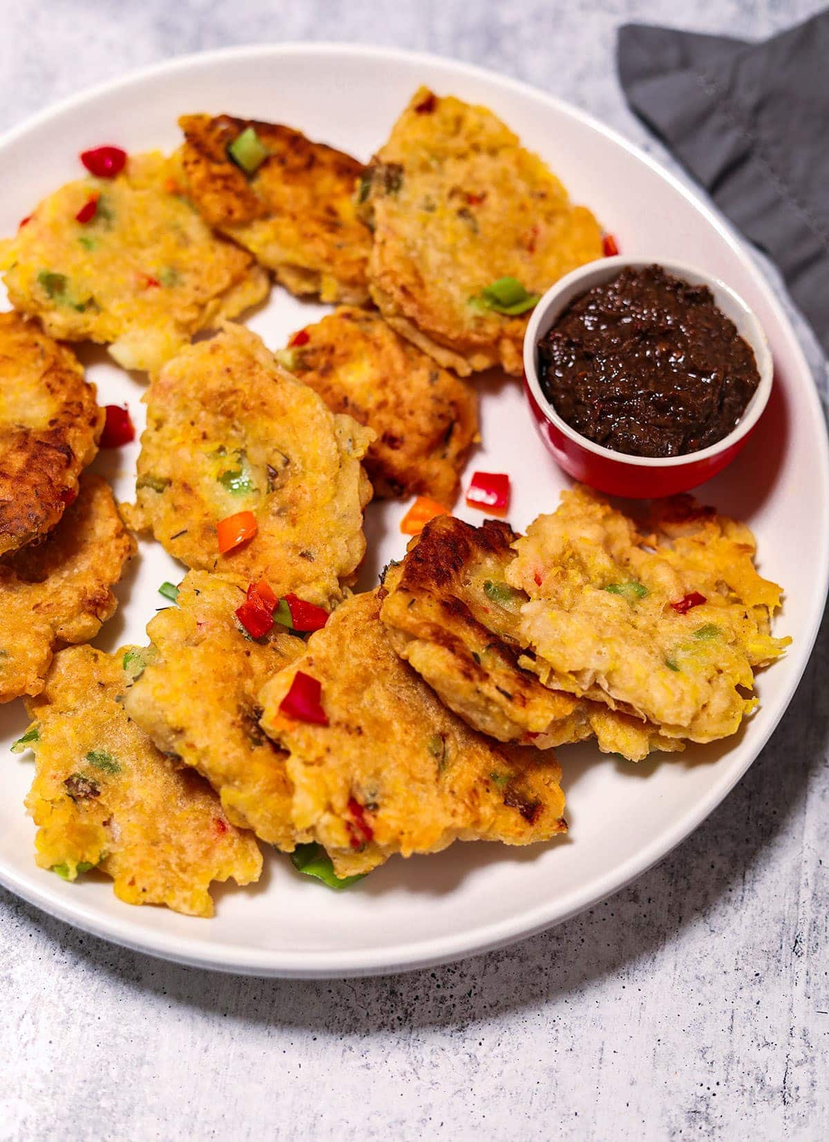 Plantain fritters overlay in a white plate with jerk sauce in a small bowl