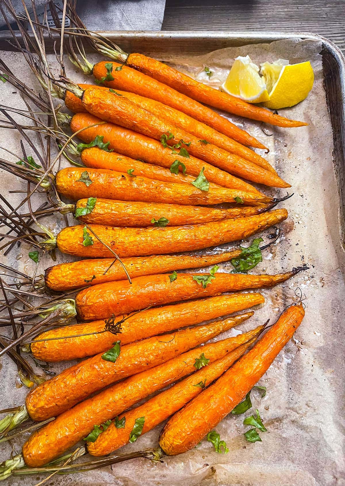 a sheet pan with parchment paper and a row of air fried carrots garnished with parsley and lemon