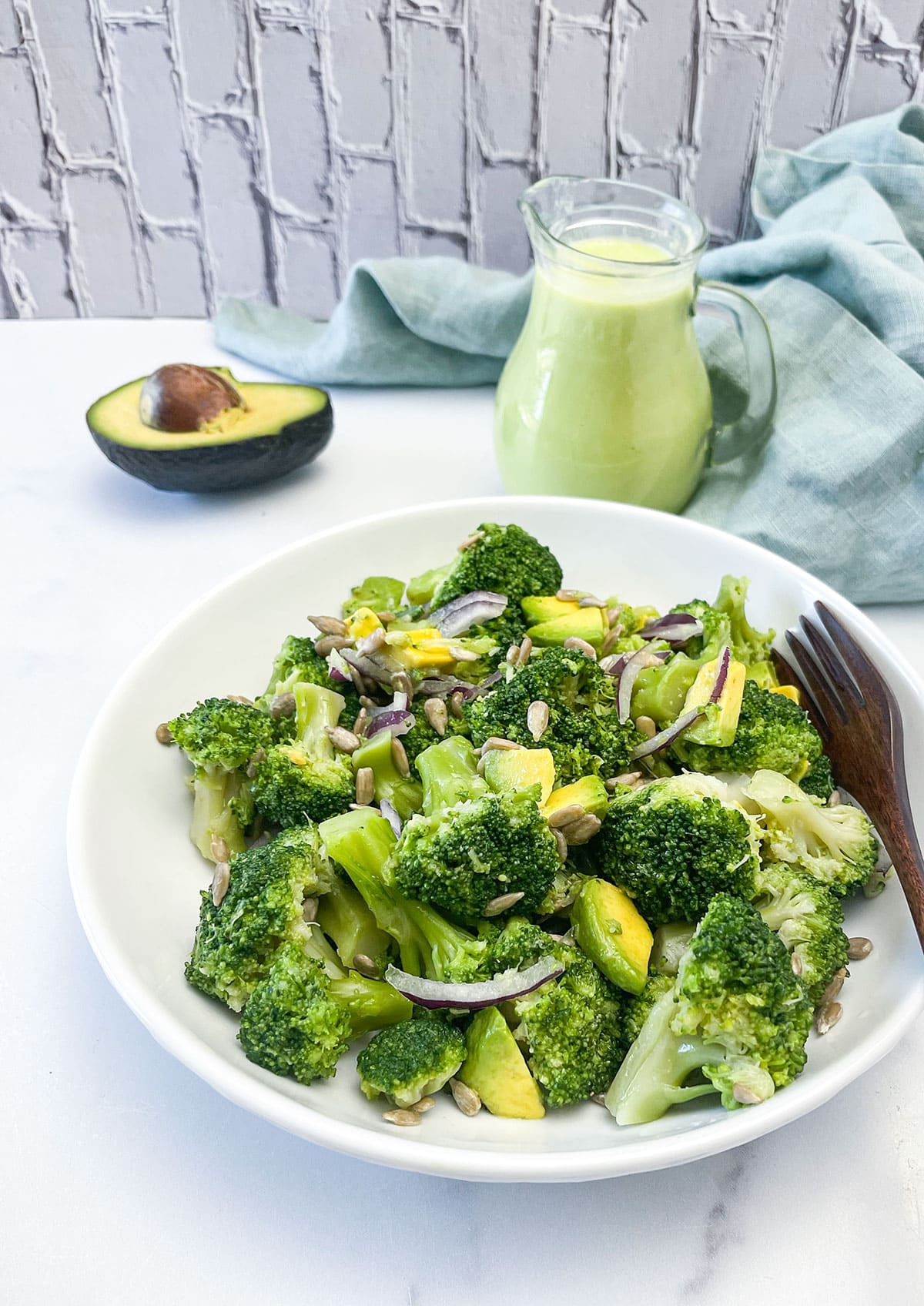 broccoli salad on a white plate with a salad dressing in the background and avocado