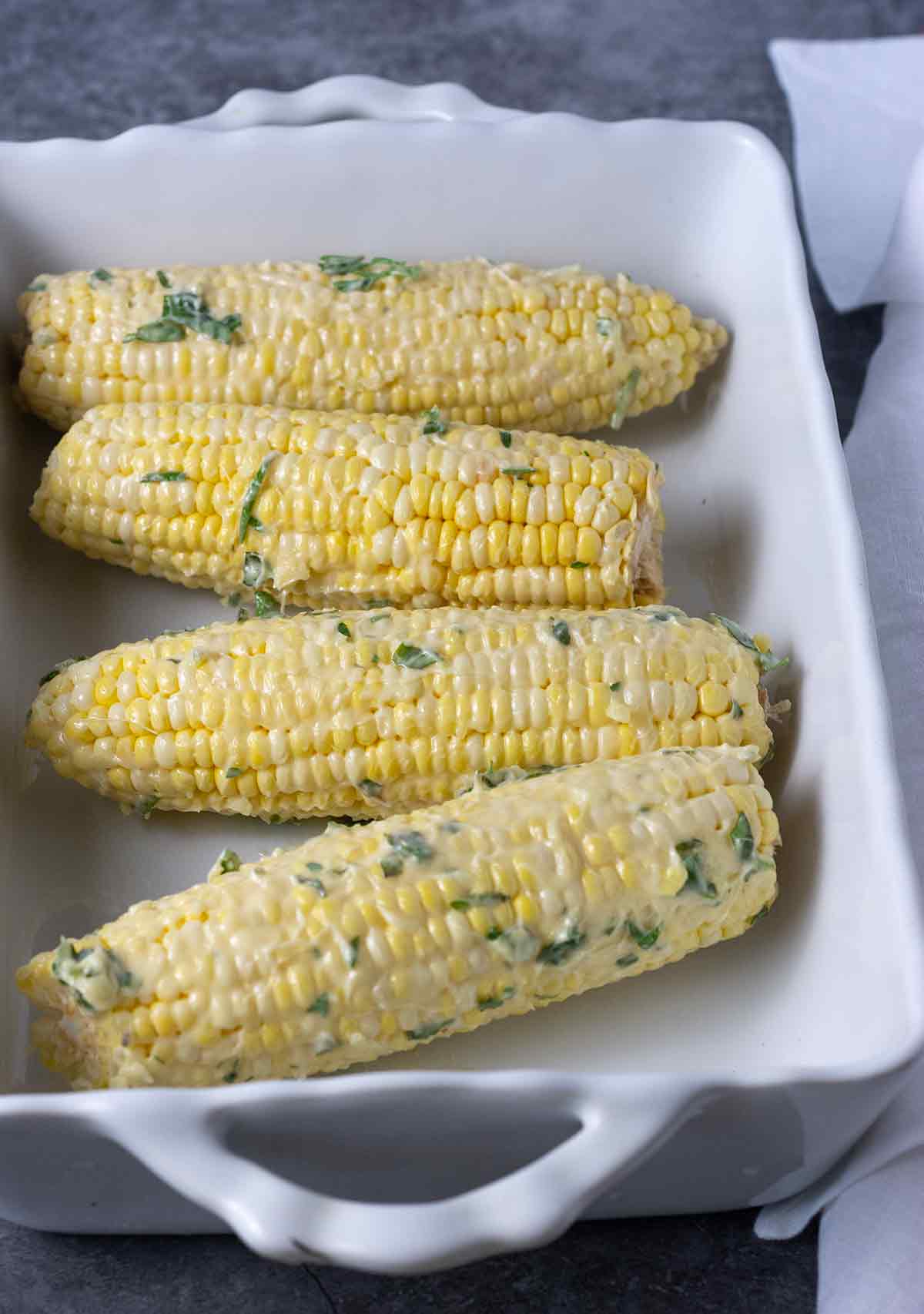 Overlay of corn smothered with vegan butter and herbs in a white baking dish