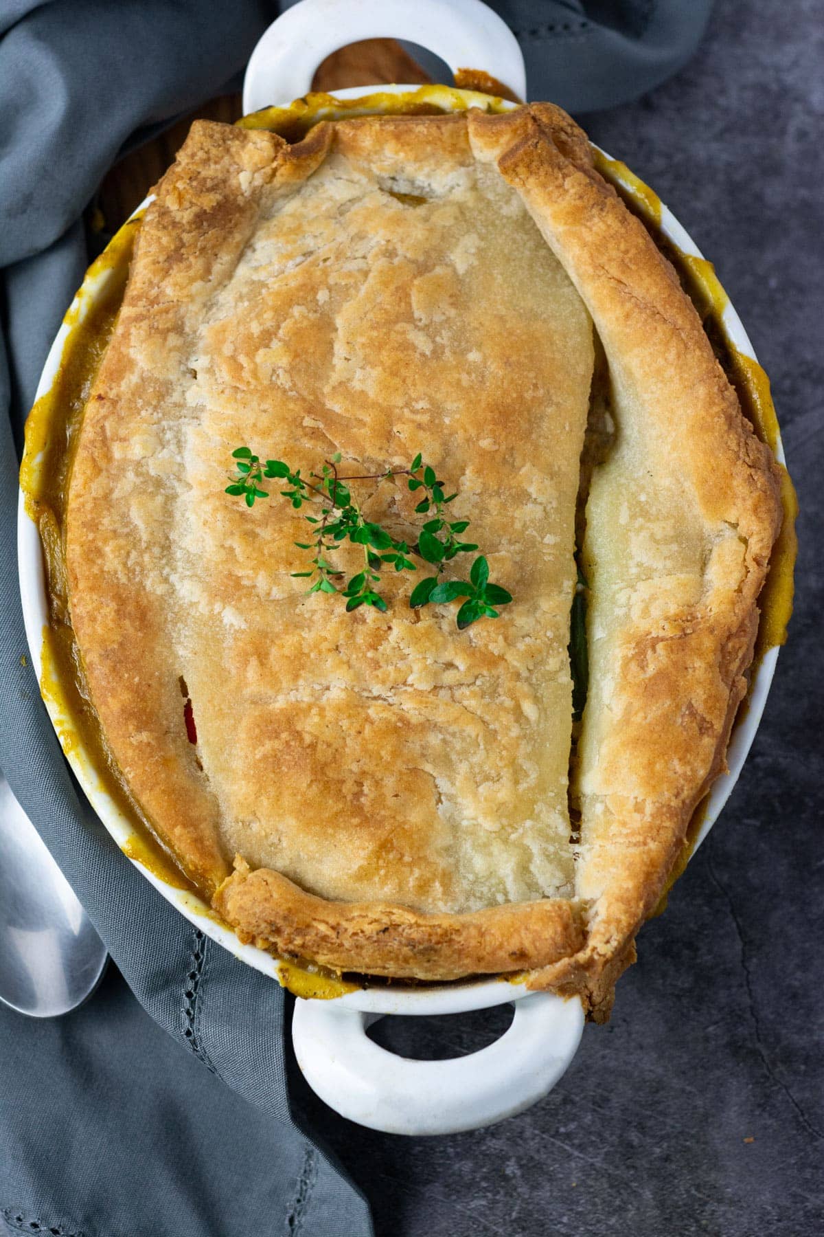 Overlay gluten-free vegan pot pie in a white casserole dish with gluten-free pie crust garnished with fresh thyme on a grey background