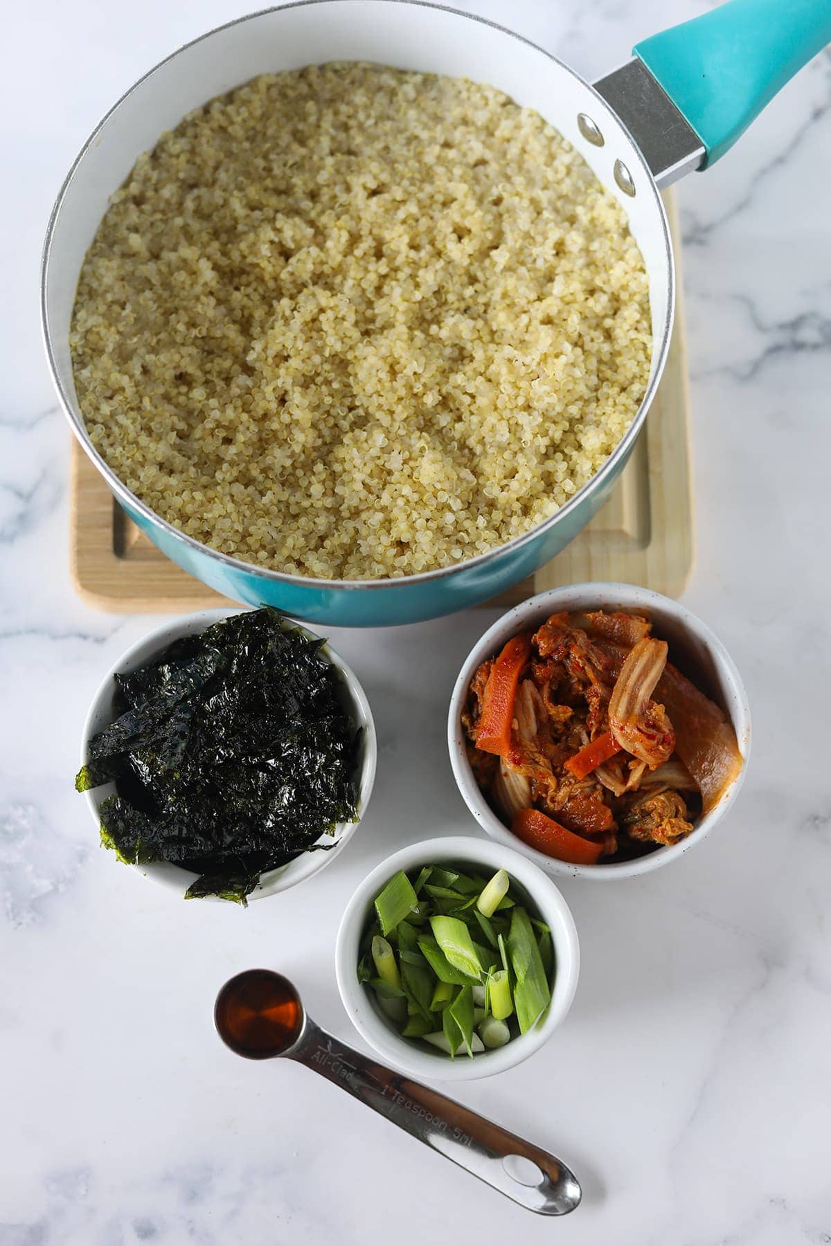 ingredients for kimchi fried rice on a white marble background, blue and white pot with quinoa, bowl with kimchi, nori, green onion, sesame oil